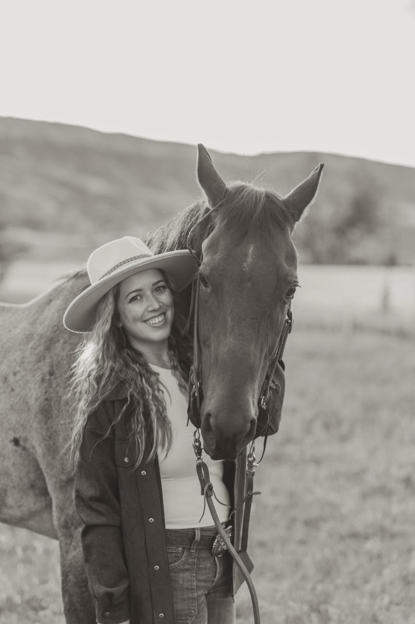 Black-and-white portrait of Sabrina Fitzgerald standing beside one of her horses.